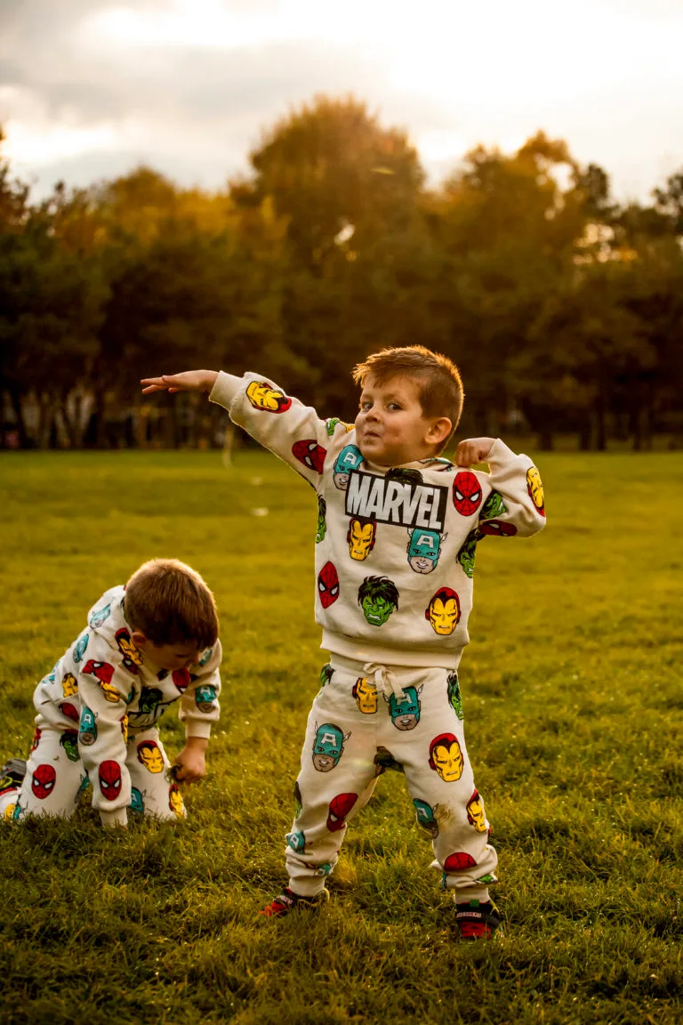 Doi frați în costume Marvel pozând în parc, ședință foto copii în lumină naturală