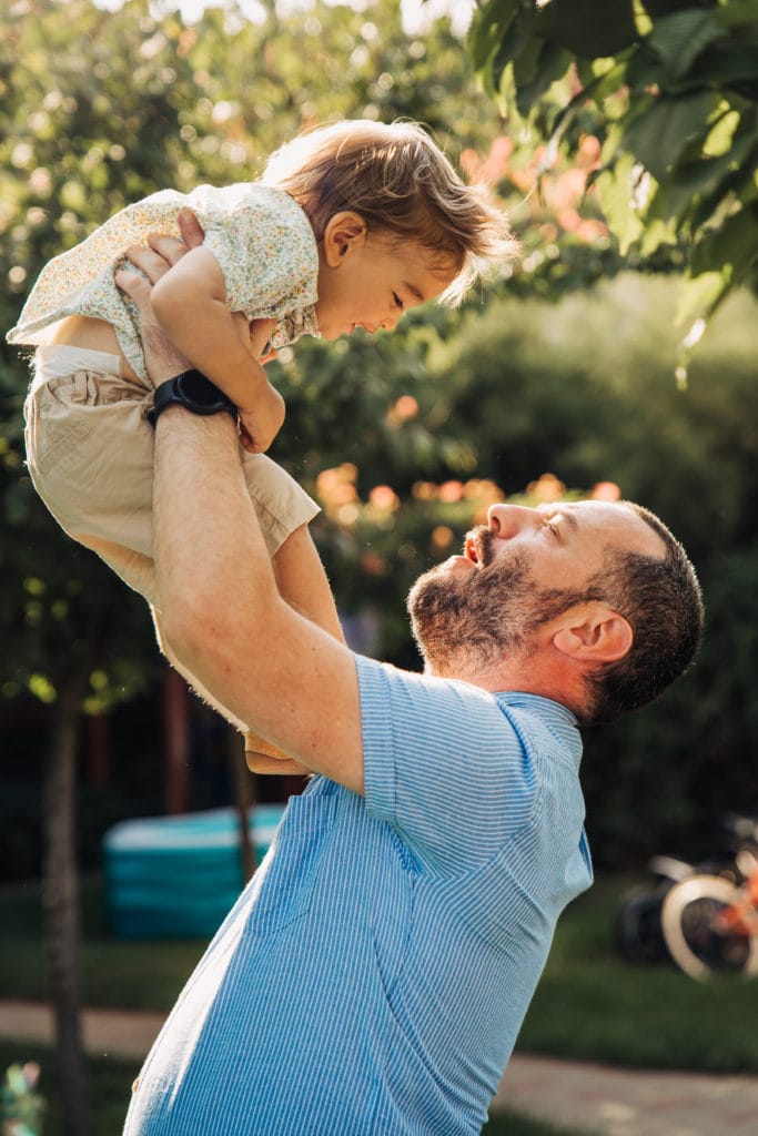 Tată ridicând copil mic în aer, ședință foto familie în exterior lumină naturală