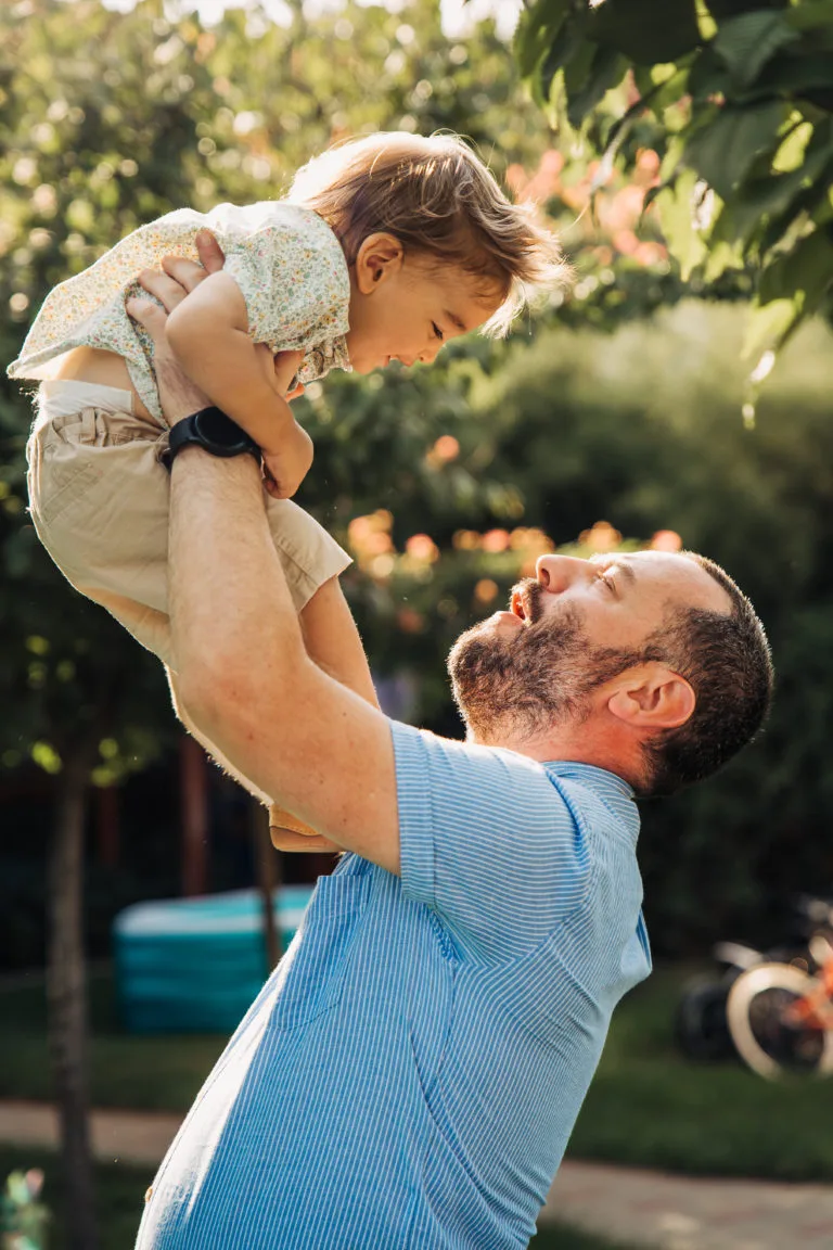 Tată ridicând copil mic în aer, ședință foto familie în exterior lumină naturală