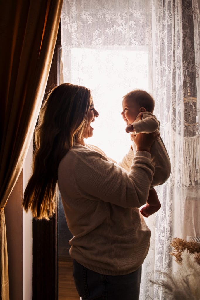 Mamă și bebeluș fericiți la fereastră, ședință foto de familie călduroasă București