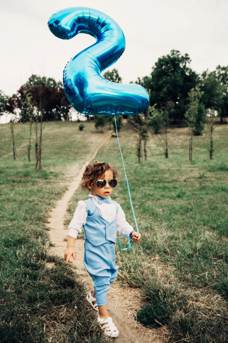Copil de doi ani cu balon albastru și ochelari de soare, ședință foto aniversară în aer liber