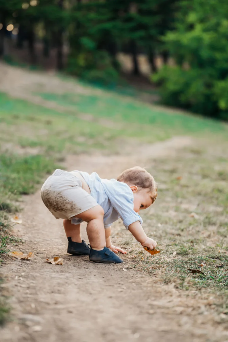 Bebeluș curios explorând frunze uscate în parc, ședință foto copii exterior