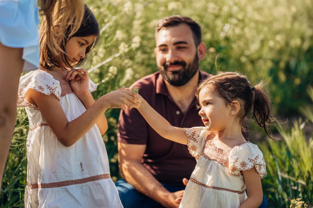 Ședință foto familie în câmp înflorit, tată și două fetițe în lumină naturală caldă
