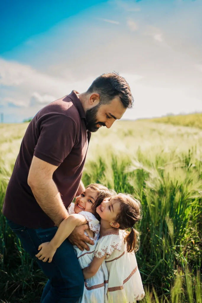Tată cu două fetițe zâmbitoare în lan de grâu, ședință foto familie în aer liber