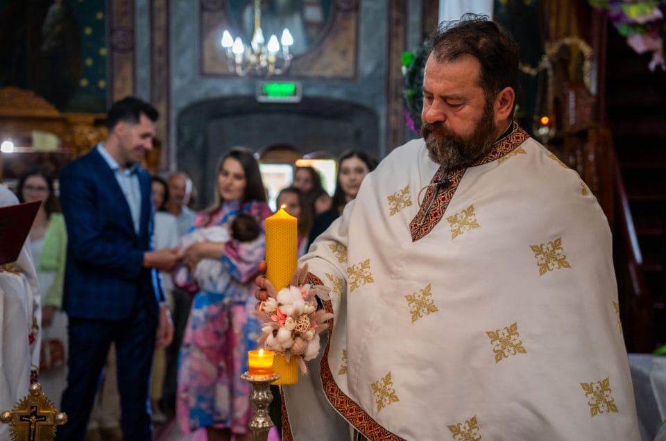 Preot ortodox cu lumânare de botez în biserică, fotografie emoționantă de botez București