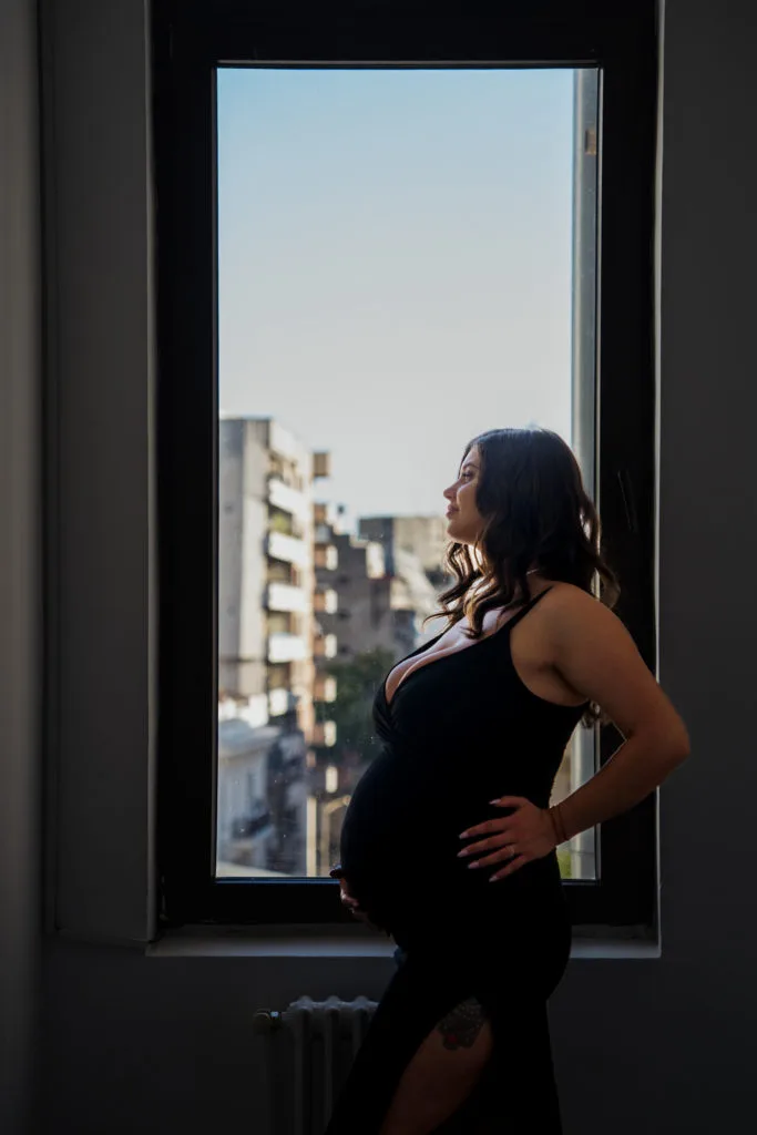Femeie însărcinată în rochie neagră la fereastră, ședință foto maternitate București