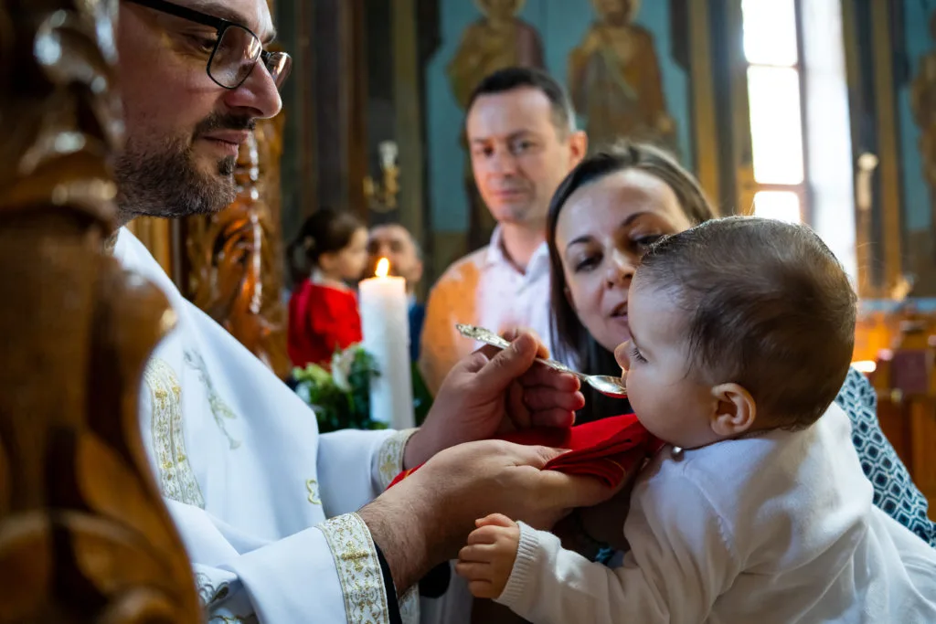 Preot administrând împărtășania bebelușului la botez în biserică ortodoxă