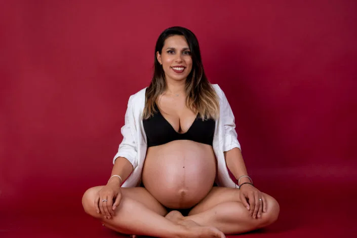 Femeie însărcinată așezată în studio, ședință foto maternitate București fond roșu