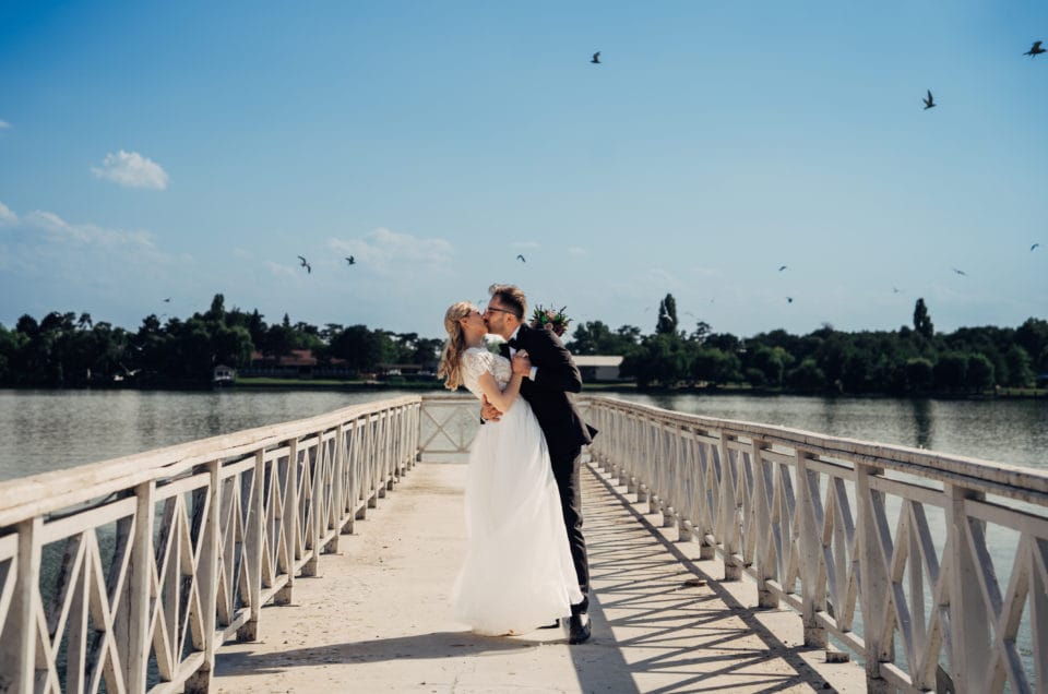 Cuplu de miri sărutându-se pe pod deasupra lacului, fotografie romantică de nuntă