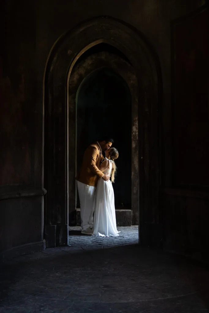 Cuplu de miri sărutându-se în arcadă istorică, fotografie de nuntă cu lumină dramatică