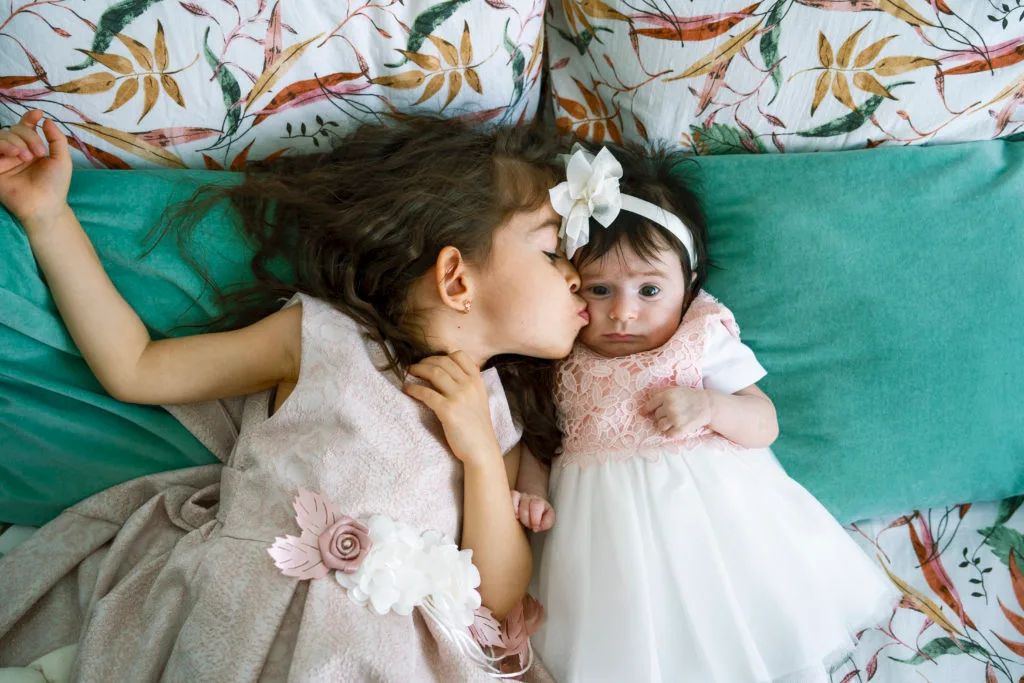 Surioară sărutând bebelușul la fotografie de botez, rochițe roz delicate