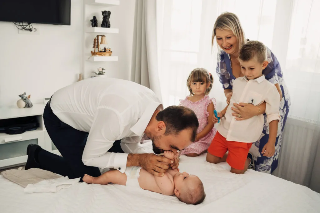Tată sărutând picioarele bebelușului, ședință foto familie emoționantă în interior