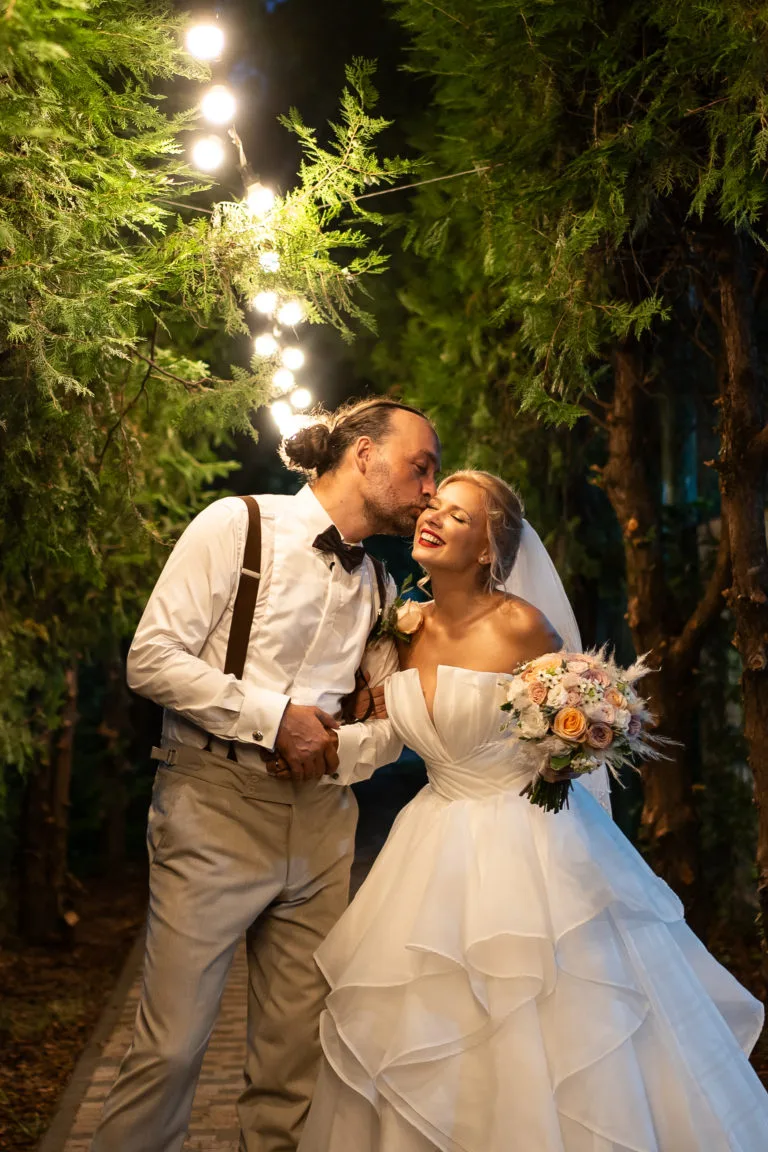 Miri sărutându-se romantic noaptea în parc, fotografie de nuntă cu lumini festive