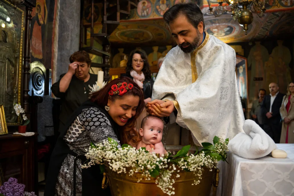 Preot botezând bebeluș în cristelniță cu flori, fotografie de botez emoționantă București