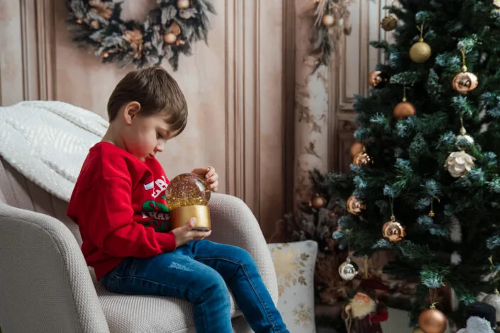 Băiat cu snow globe lângă brad împodobit, ședință foto de Crăciun în interior