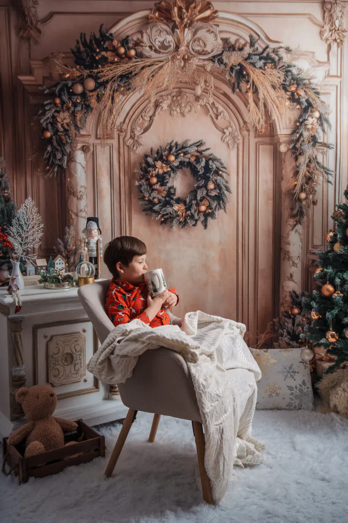 Băiat în pijamale roșii cu cană de Crăciun, ședință foto de iarnă elegantă
