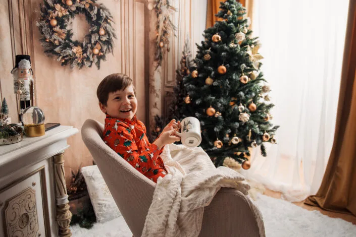 Băiat zâmbind în fotoliu lângă brad împodobit, ședință foto de Crăciun