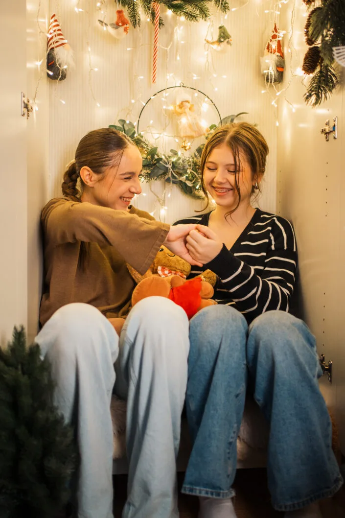 Două fete zâmbind în ședință foto de Crăciun cu decoruri festive și luminițe