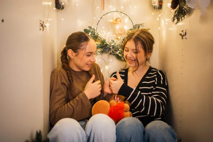 Două prietene zâmbind într-o ședință foto de Crăciun cu lumini festive