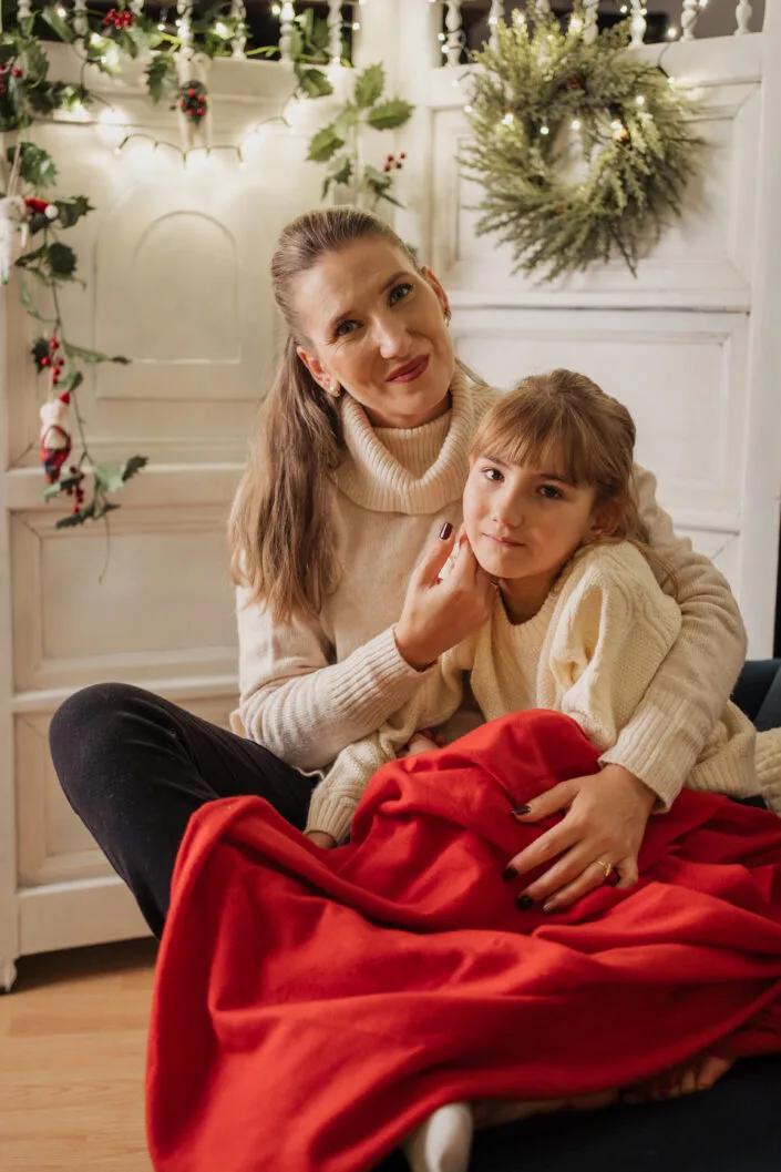 Ședință foto familie de Crăciun mamă și fiică în pulovere crem cu pătură roșie