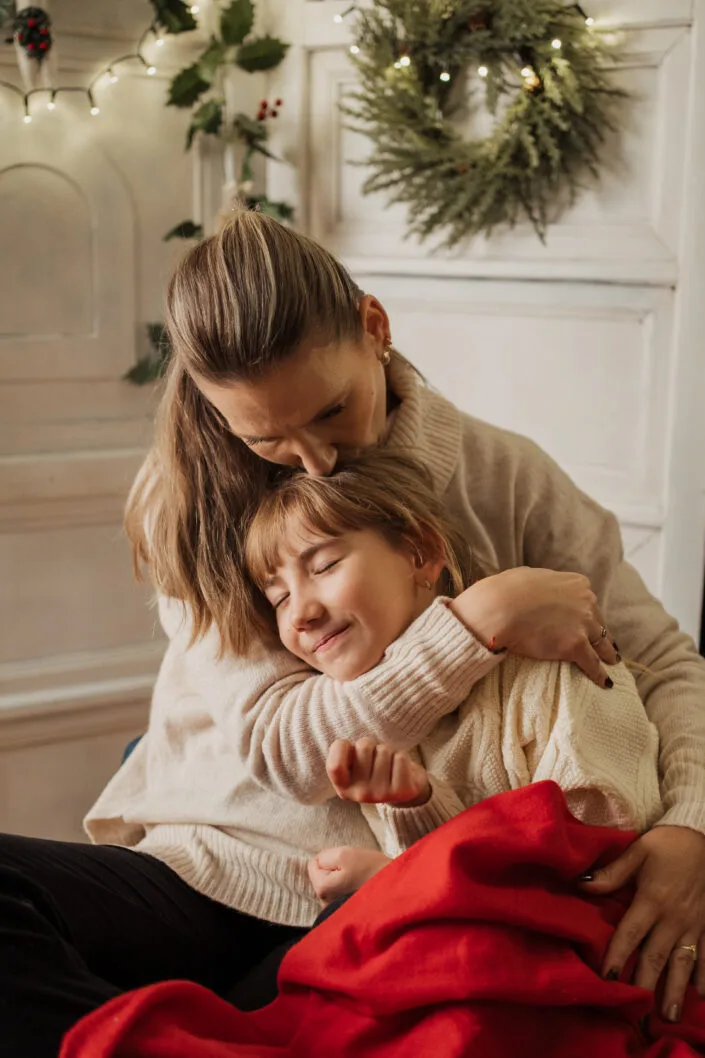 Mama îmbrățișând copilul cu drag, ședință foto familie atmosferă caldă de Crăciun