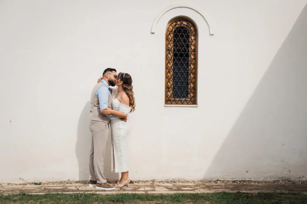 Miri sărutându-se lângă biserică albă, fotografie de nuntă elegantă București