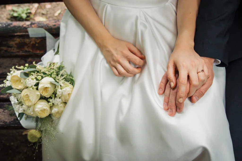 Mâinile mirilor împreunate pe rochie albă cu buchet de trandafiri, fotografie elegantă de nuntă București