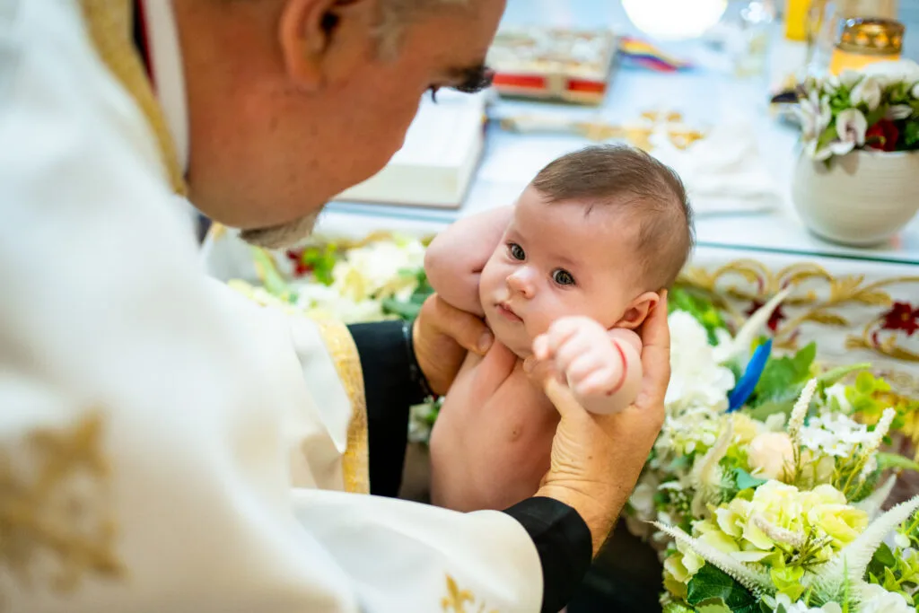 Preot ținând bebeluș la botez lângă altar, fotografie emoționantă București