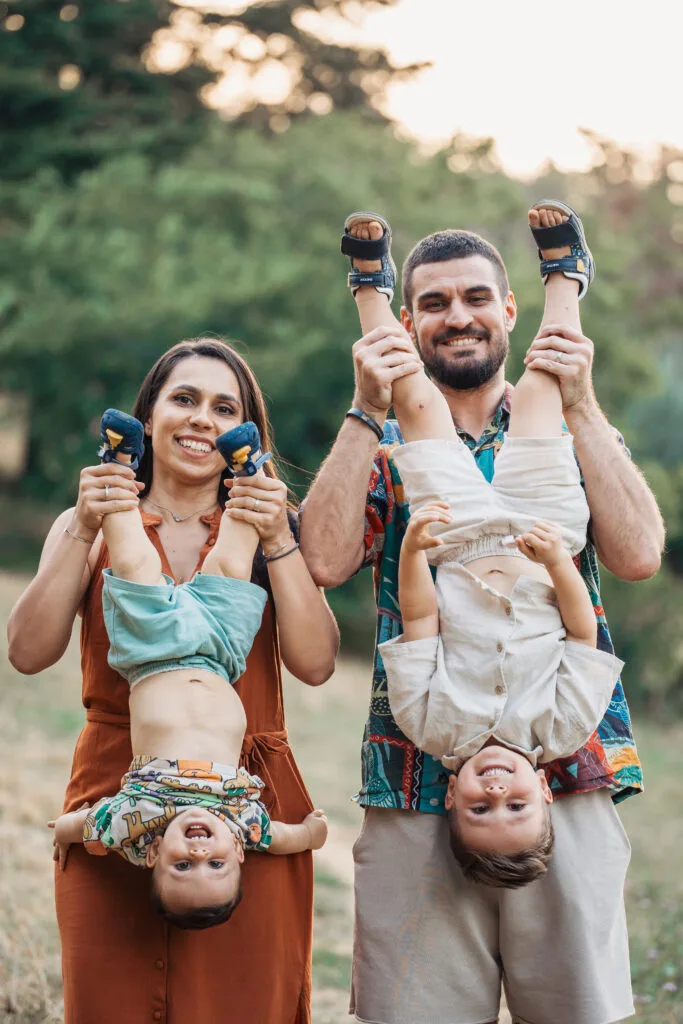 Familie fericită cu doi copii ținuți invers, ședință foto exterior București